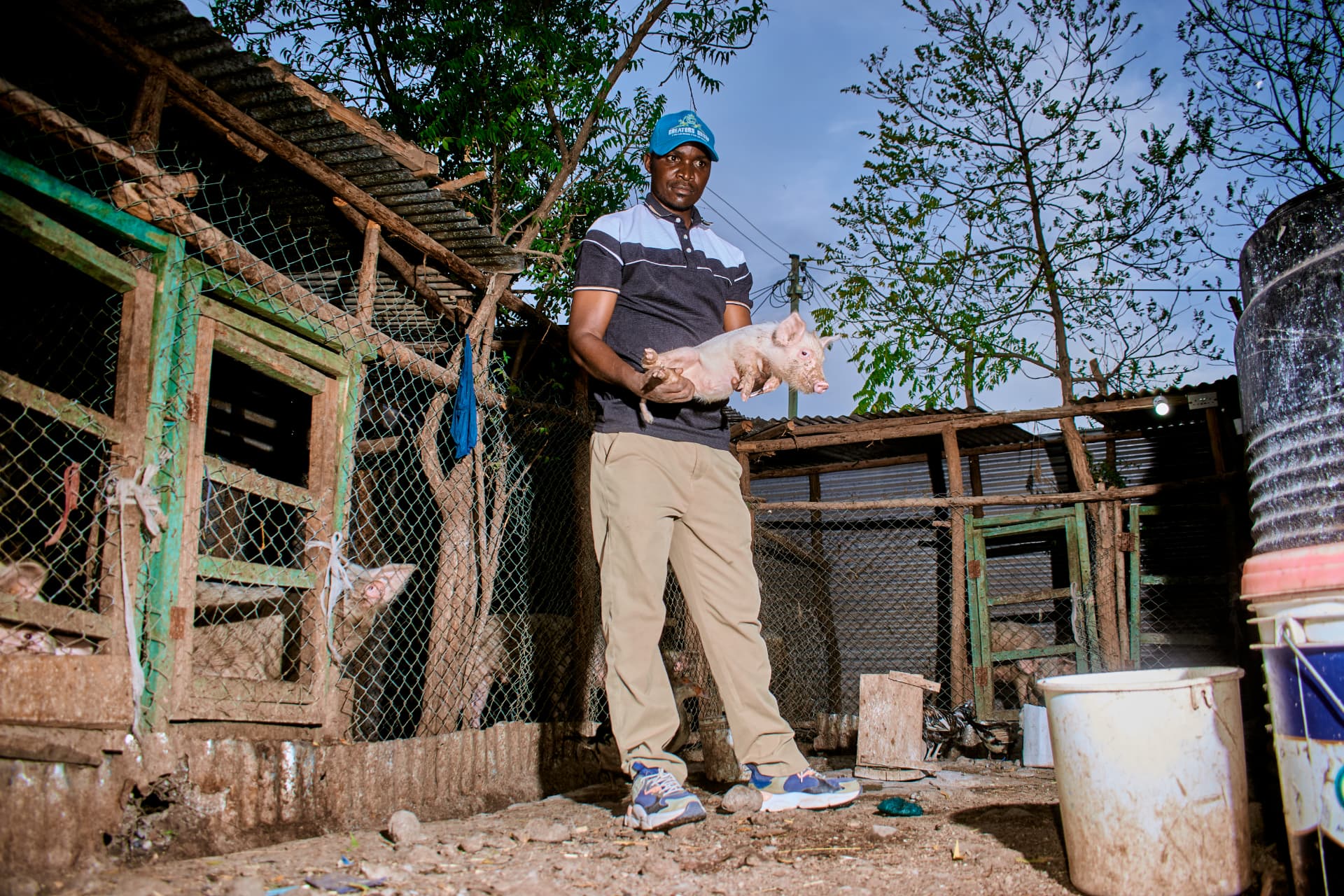 Celestin holding a piglet beside the pig enclosures